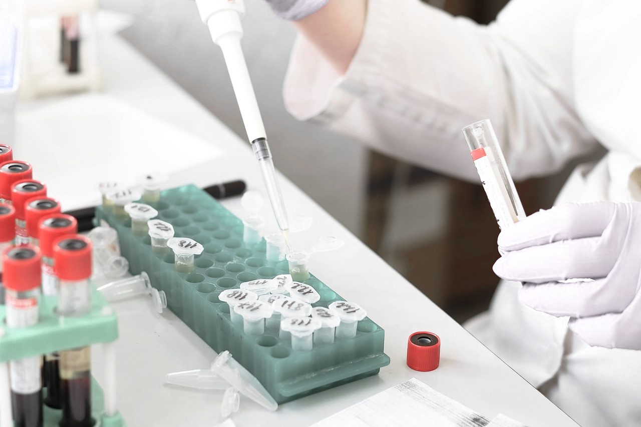 Gloved hand pipetting samples into tubes at a laboratory bench